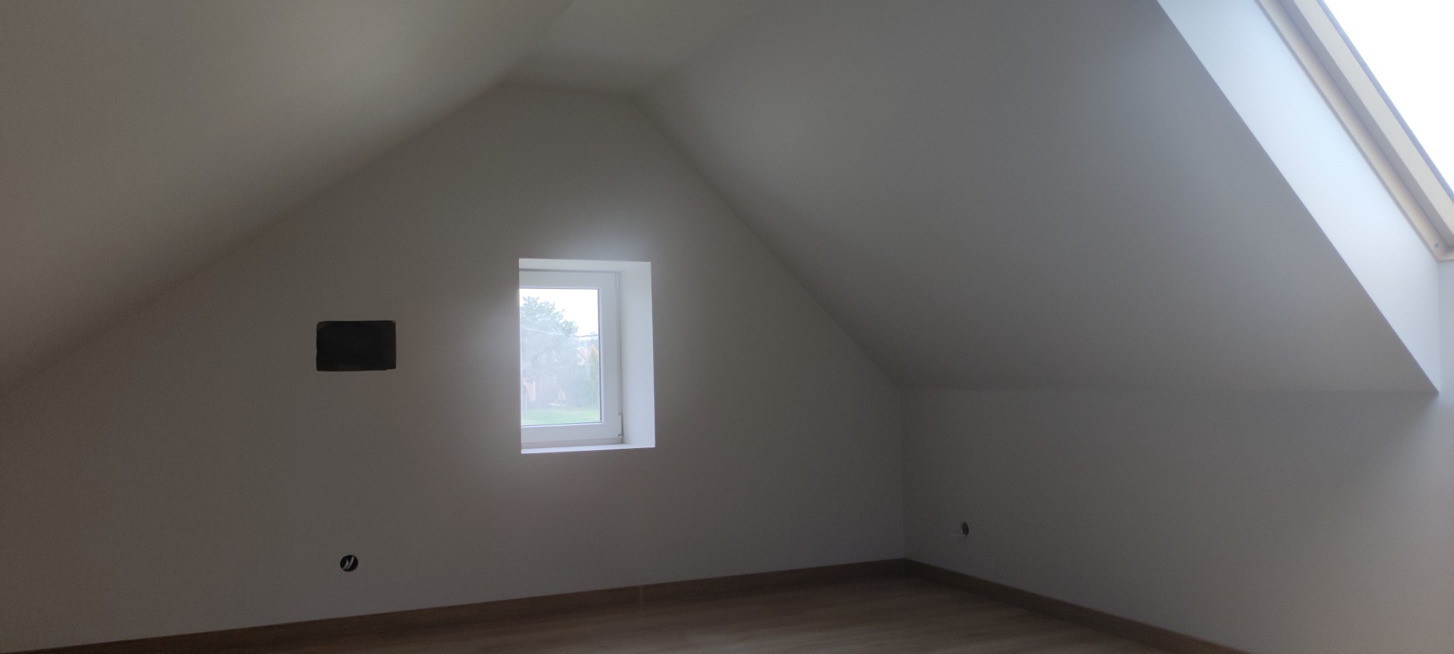 Poddasze po remoncie, ściany pomalowane na biało, widoczne okno dachowe i okno w ścianie szczytowej, przygotowane miejsce na gniazdko elektryczne i otwór na puszkę elektryczną.