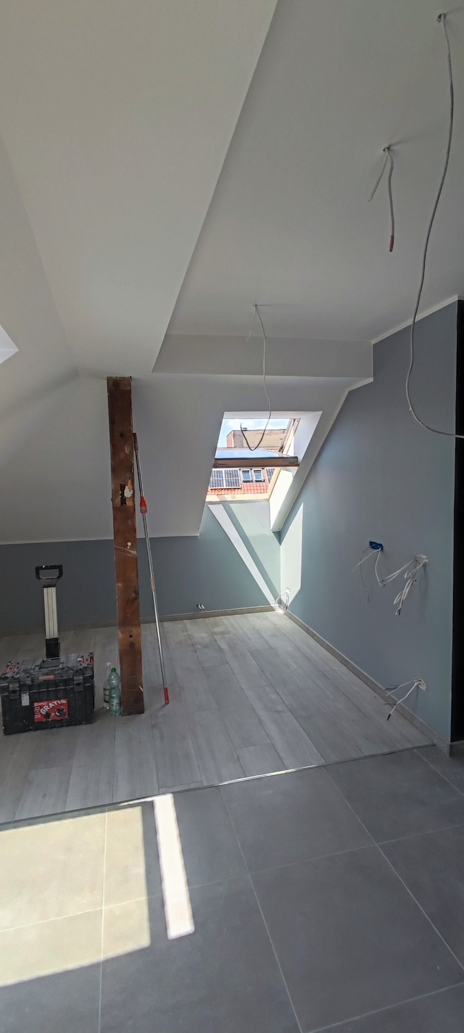 Poddasze po remoncie z widocznymi elementami instalacji elektrycznej, skrzynką narzędziową i otwartym oknem dachowym.