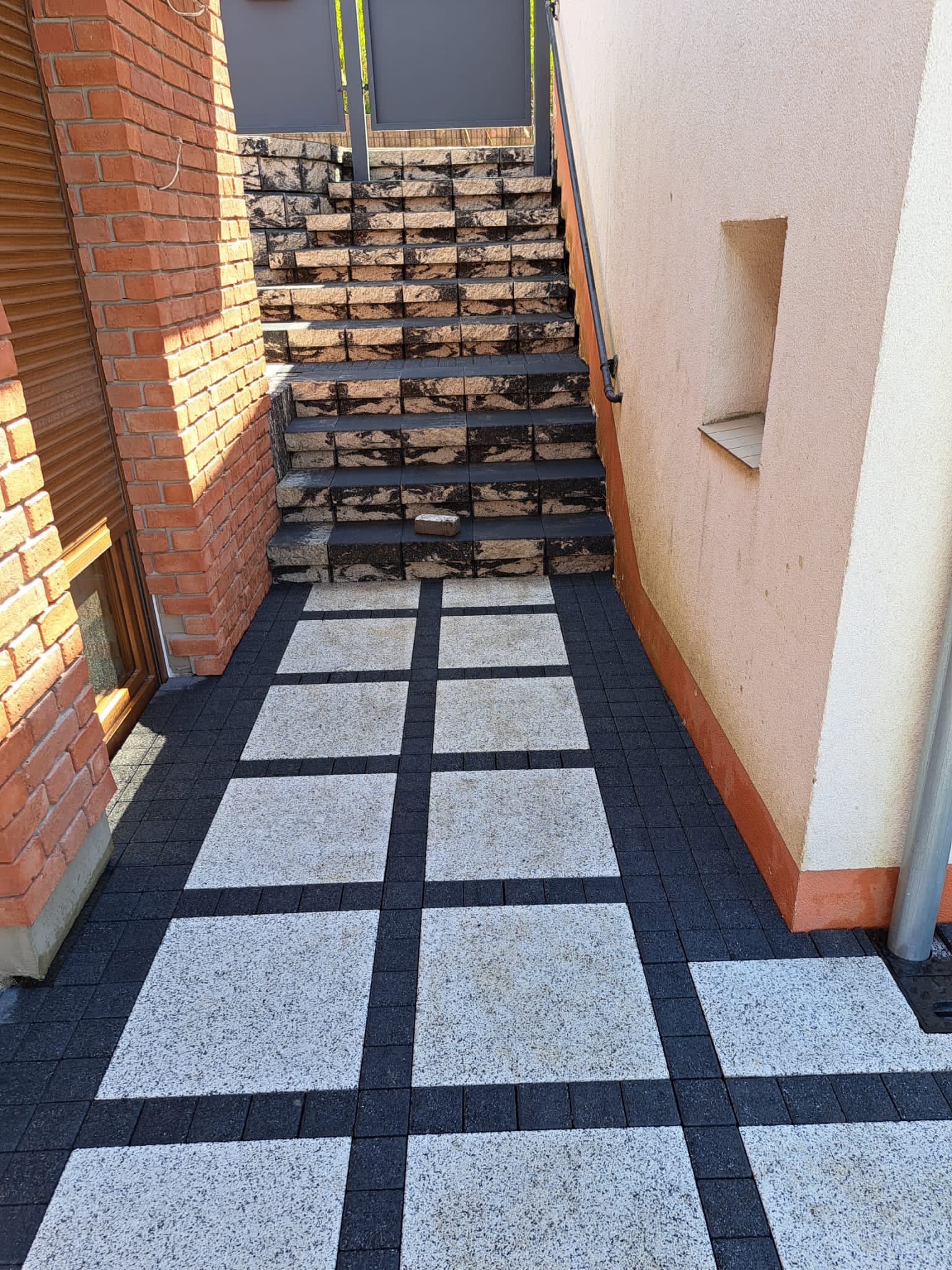 Ułożona nawierzchnia z kostki brukowej w Bytnicy, tworząca wzór kwadratów z jasnej kostki otoczonej ciemną kostką, prowadząca do schodów z kamienia.