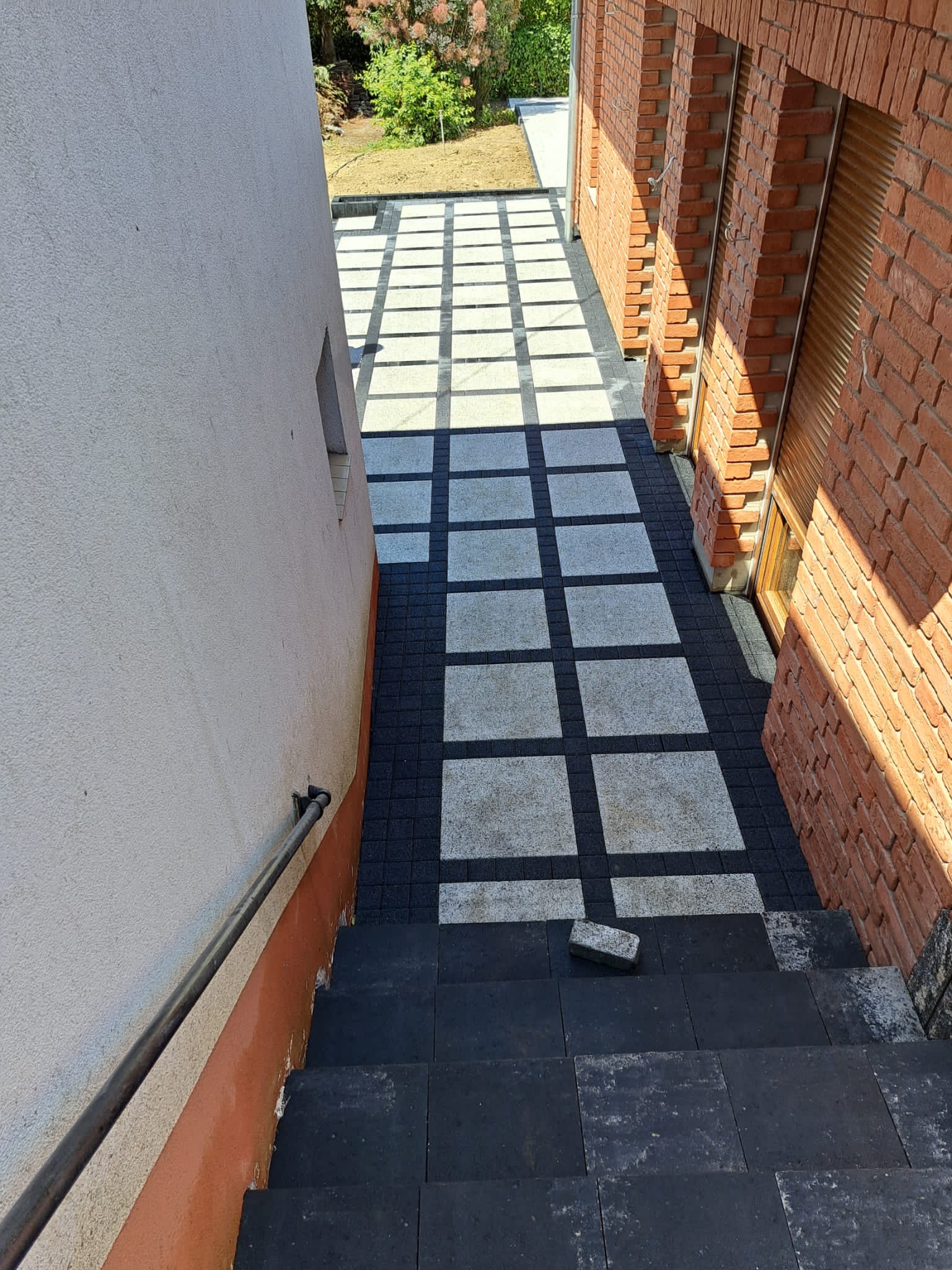 Schody wyłożone czarną kostką brukową prowadzą do wzoru z szarej kostki ułożonej w kwadraty oddzielone czarną kostką, widok z góry.