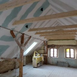 Mar-Regips - Poddasze w trakcie adaptacji: widoczne drewniane belki stropowe, częściowo zamontowane płyty na ścianach ze śladami szpachlowania, ocieplenie wełną mineralną w przestrzeniach między krokwiami,...