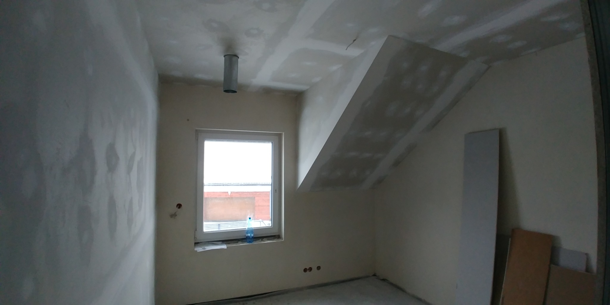 Pokój w trakcie prac wykończeniowych: ściany wstępnie wyszpachlowane, sufit z zamontowaną płytą gipsowo-kartonową, widoczne ślady szpachli, okno z butelką wody na parapecie, przygotowane płyty...