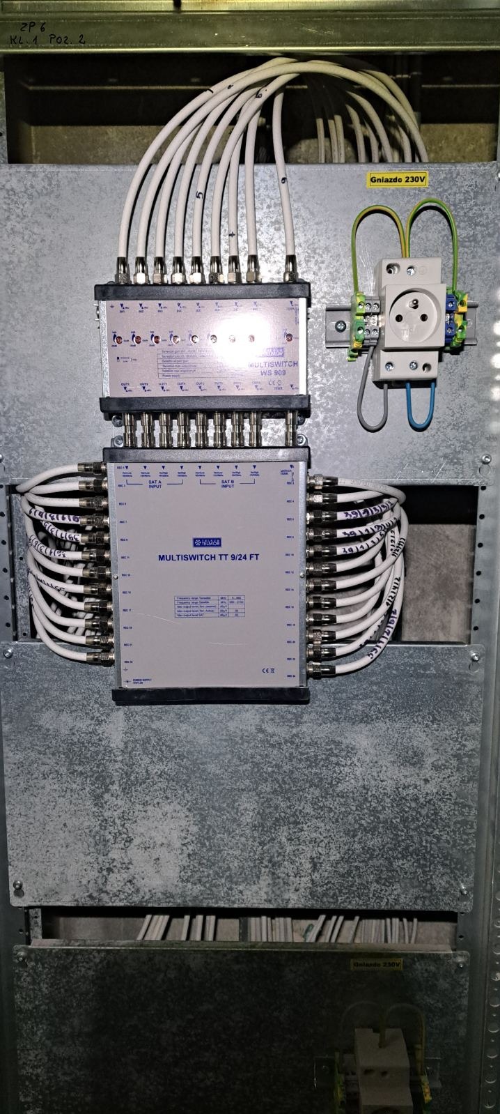 Rozdzielnica multiswitch z podłączonymi kablami koncentrycznymi i gniazdem 230V, widoczne numery identyfikacyjne na kablach.