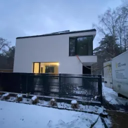 Nowoczesny dom jednorodzinny z płaskim dachem, ocieplany z użyciem węża podłączonego do pojazdu firmy PUR Solutions, widok z zasypanego śniegiem ogrodu.