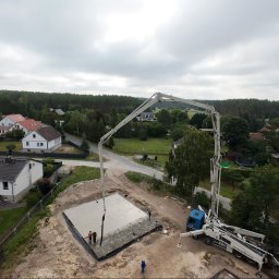 BOEK usługi budowlane Eduard Krynitski - Betonowanie fundamentu domu jednorodzinnego z użyciem pompy do betonu. Widok z góry na plac budowy w otoczeniu zabudowy mieszkalnej i lasu, pochmurne niebo.