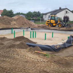 BOEK usługi budowlane Eduard Krynitski - Fundamenty domu w trakcie budowy, widoczny wykop, izolacja, rury pionowe i koparka JCB w tle. Teren przygotowany pod wylewkę.