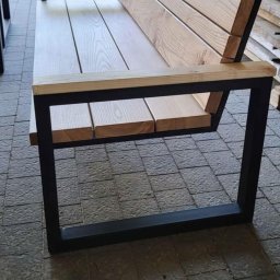 Mebelq - Drewniana ławka ogrodowa z metalową ramą, widoczna na tle ułożonego drewna i roweru, na szarym brukowanym patio.