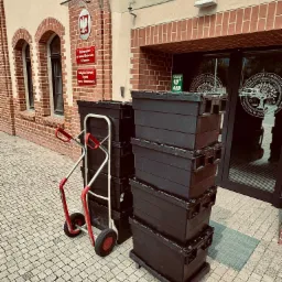 Stos czarnych skrzyń na wózku transportowym przed budynkiem Wydziału Prawa i Administracji UAM w Poznaniu. Przygotowania do przeprowadzki.