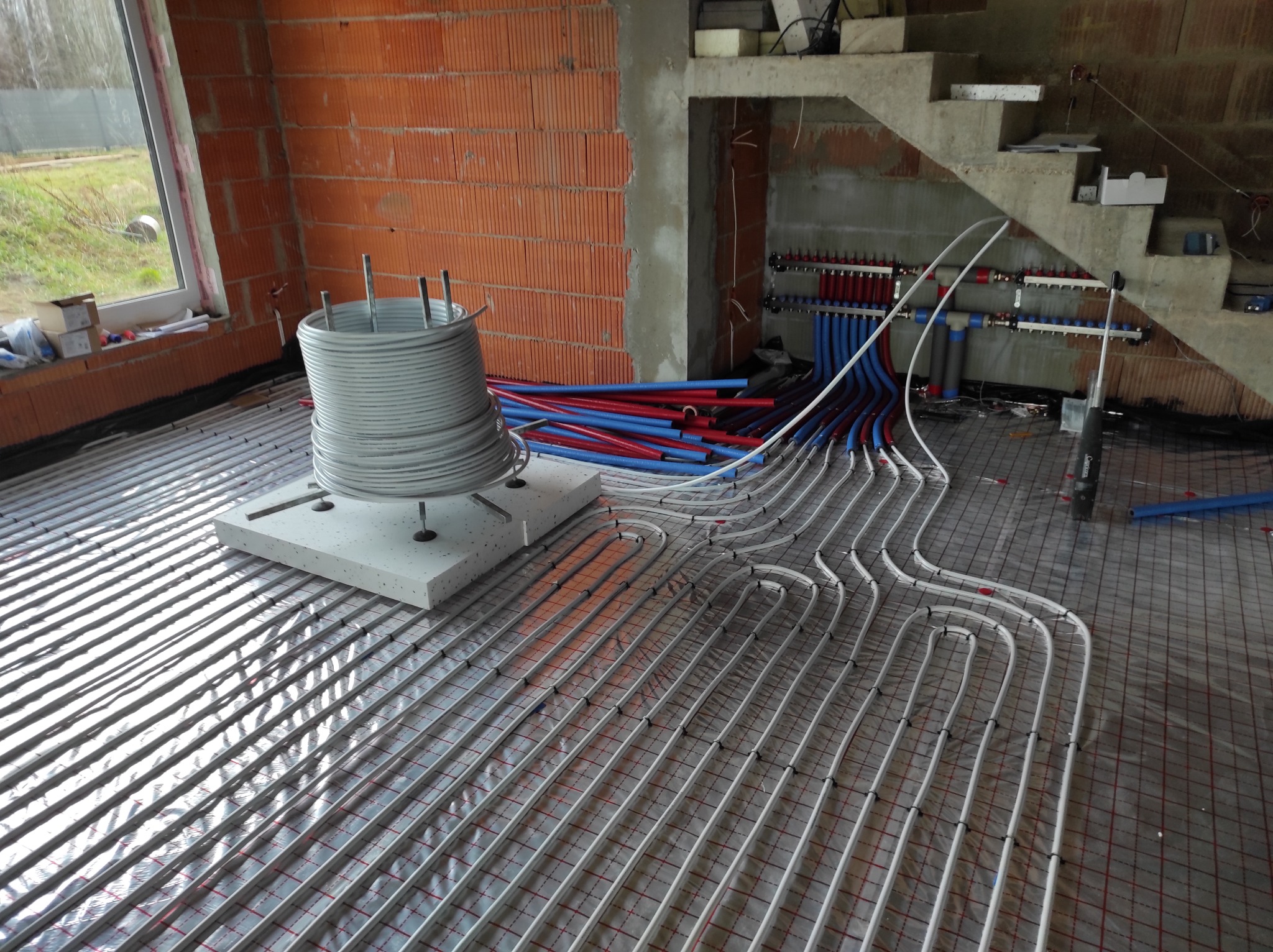 Wnętrze w Kutnie w trakcie montażu systemu rur grzewczych podłogowych, z widoczną rozdzielnią i izolacją pod wylewkę, w surowym stanie deweloperskim.
