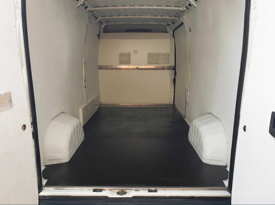 Pusta przestrzeń ładunkowa białego furgonetki z otwartymi drzwiami, widok z tyłu, czarna podłoga. Ściany wewnętrzne wyłożone białą płytą.