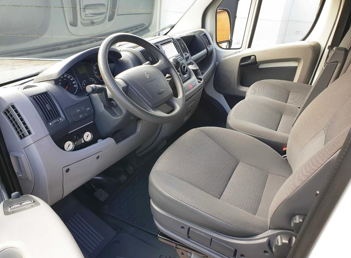 Wnętrze kabiny busa marki Citroen z szarymi fotelami, widok z perspektywy pasażera na deskę rozdzielczą, kierownicę z logo i gumowe dywaniki.