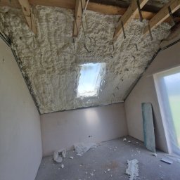 Firma Ogólnobudowlana Michał Łazowski - Poddasze po ociepleniu pianką PUR, widoczne drewniane krokwie i okno dachowe. Na podłodze resztki piany, ściany przygotowane do dalszych prac wykończeniowych.