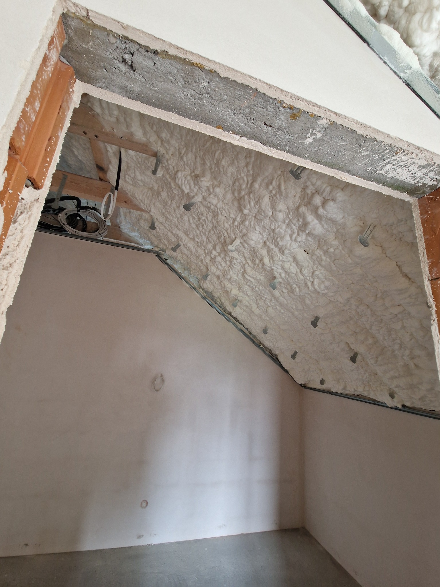 Poddasze po ociepleniu pianką PUR, widoczne elementy konstrukcyjne i instalacja elektryczna. Ściany przygotowane do dalszych prac wykończeniowych.