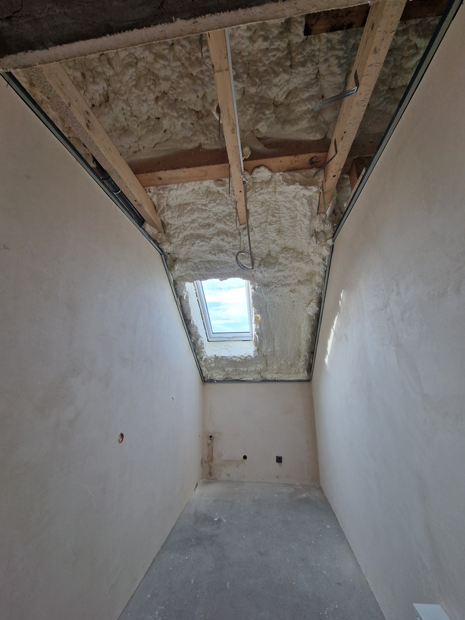 Poddasze po ociepleniu pianką PUR, widoczne drewniane elementy konstrukcyjne i okno dachowe. Ściany przygotowane do dalszych prac wykończeniowych.