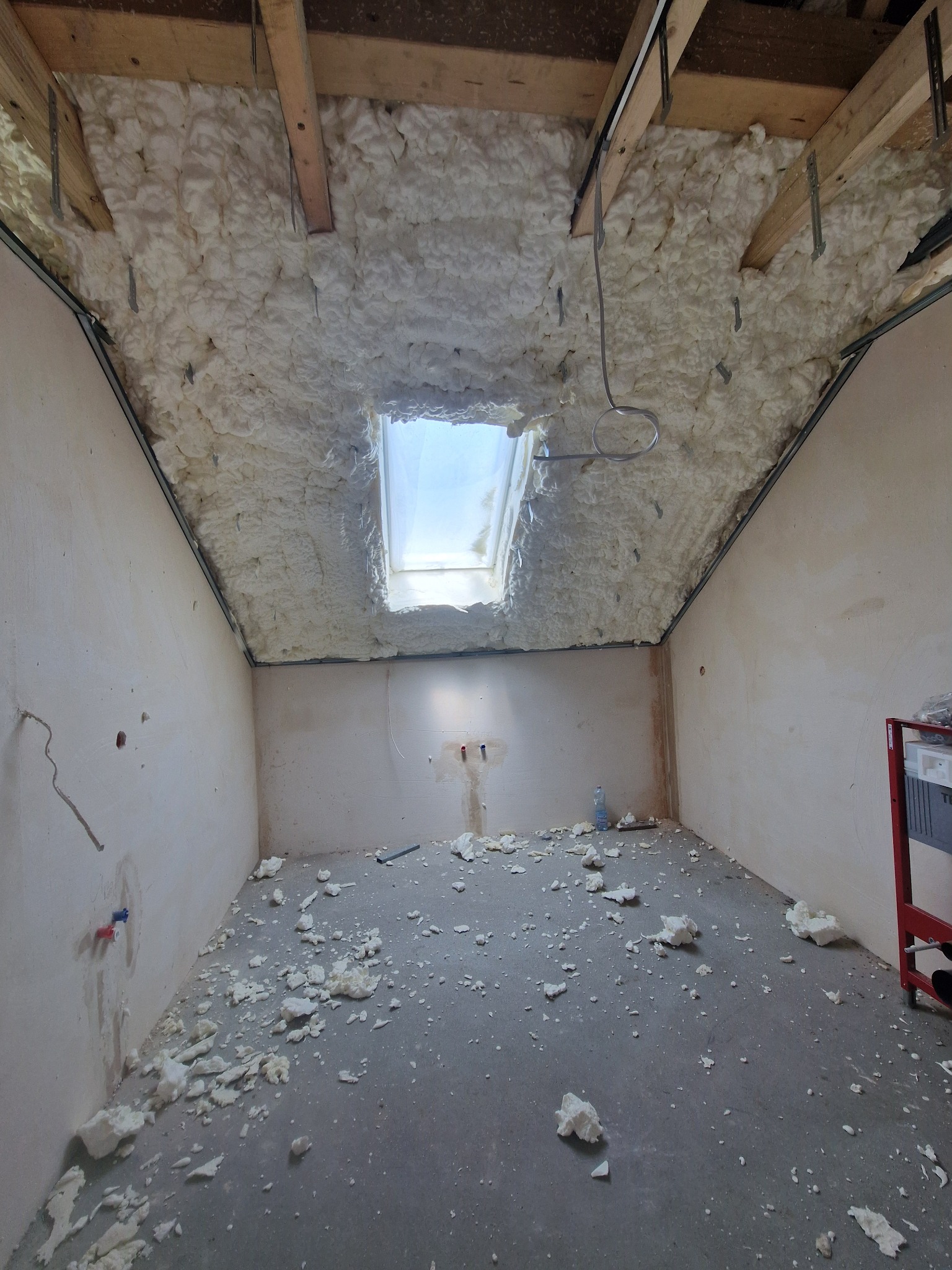 Poddasze po natrysku pianki PUR, widoczne drewniane elementy konstrukcyjne i okno dachowe. Na podłodze resztki pianki.