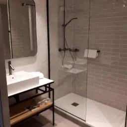 Nowoczesna łazienka z kabiną prysznicową typu walk-in, umywalką nablatową na metalowym stelażu i szarą cegłą na ścianach.