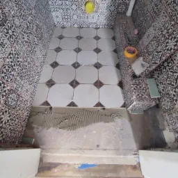 Układanie wzorzystych płytek podłogowych i ściennych w łazience, widoczna zaprawa klejowa na podłodze, plastikowe krzyżyki dystansowe i narzędzia glazurnicze.