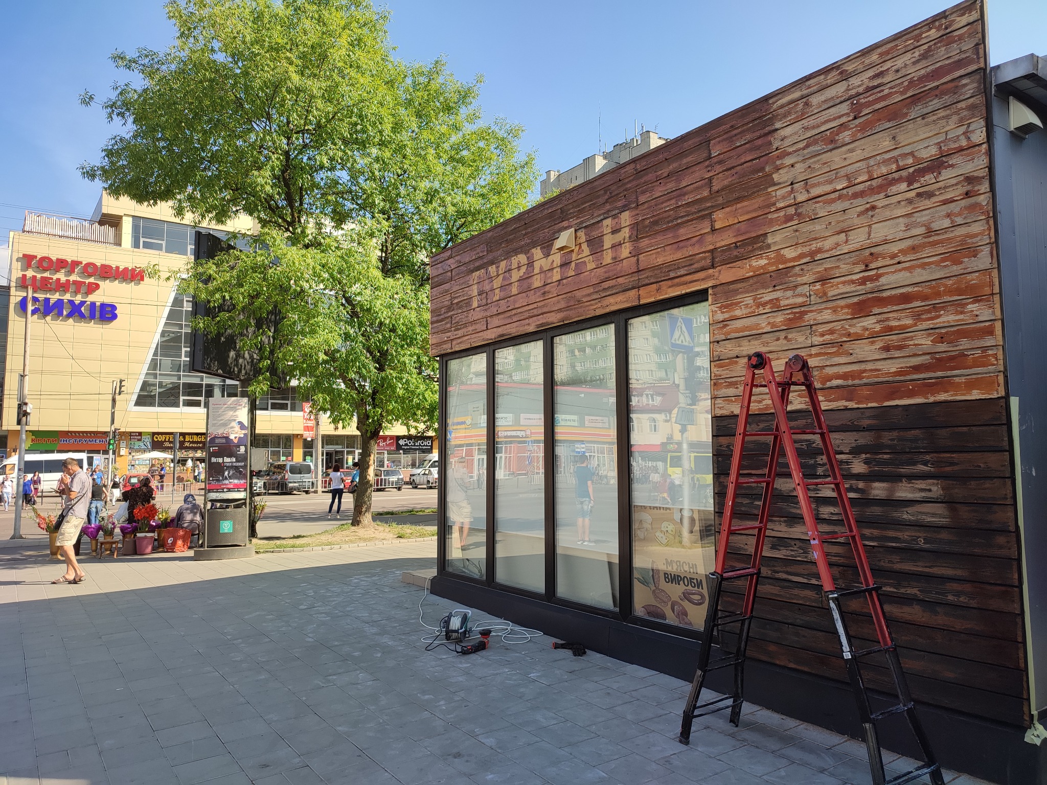 Renowacja drewnianej elewacji budynku z widoczną czerwoną drabiną, narzędziami i częściowo odnowioną powierzchnią.