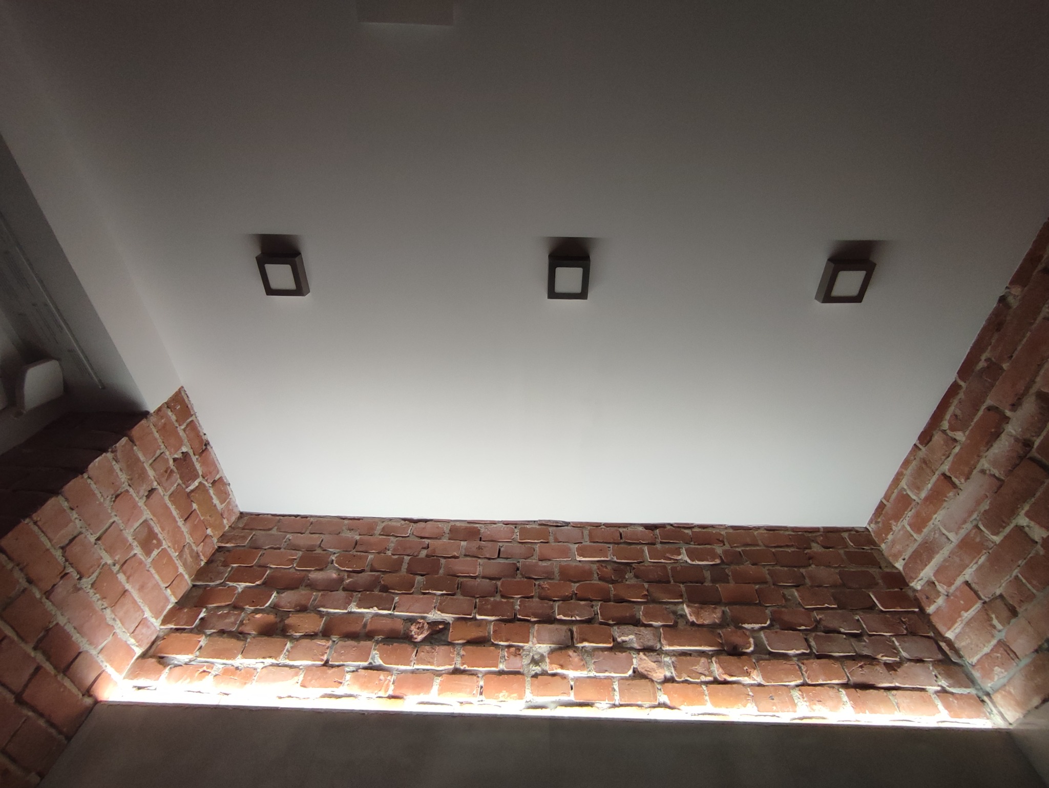 Ceglana ściana z trzema kwadratowymi lampami sufitowymi w nowoczesnym wnętrzu.