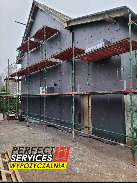 Budynek w Pszczółkach w trakcie ocieplania, widoczne rusztowania i czarne płyty izolacyjne na ścianach.