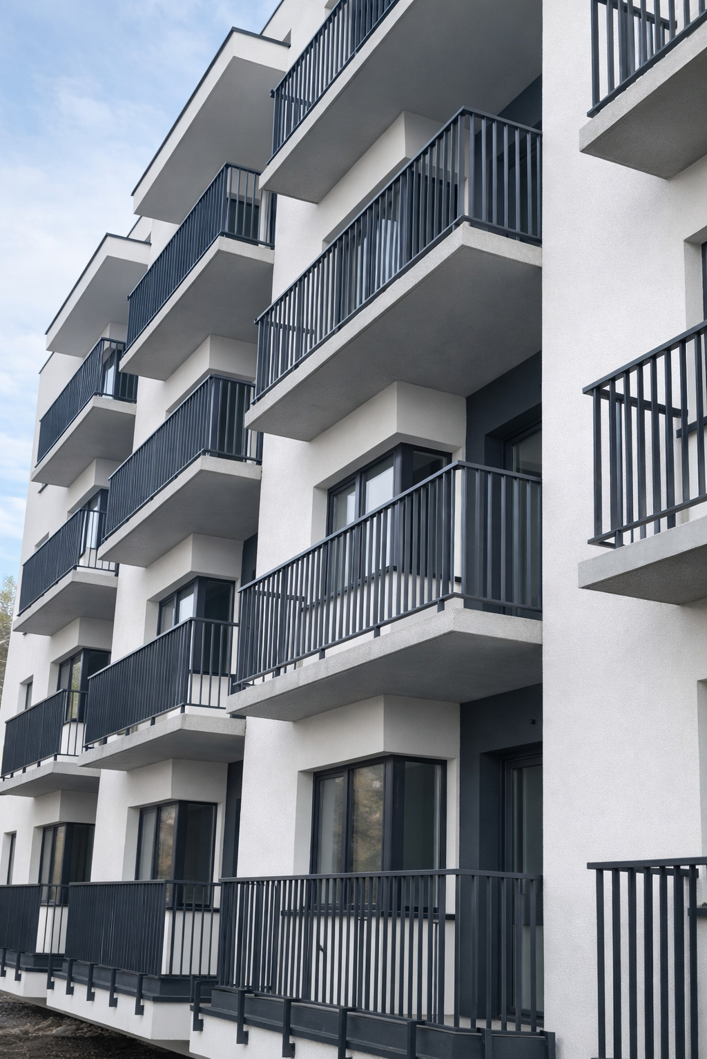 Nowoczesny budynek z balkonami zabezpieczonymi czarnymi, metalowymi balustradami. Minimalistyczny design, jasna elewacja, regularny układ balkonów.