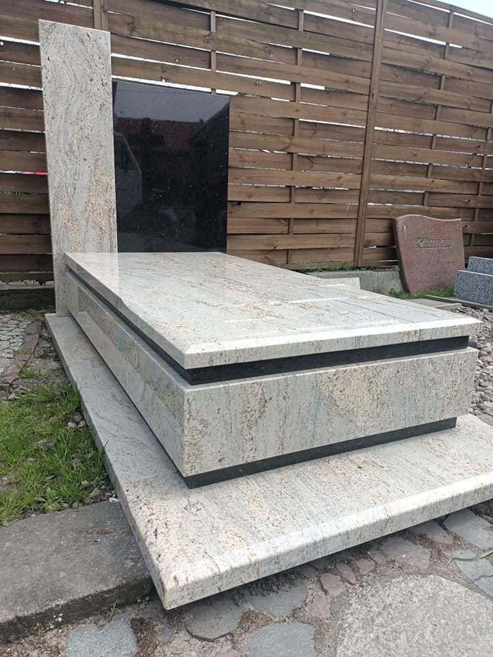 Jasny, granitowy nagrobek z czarną tablicą, ustawiony na cmentarzu z drewnianym płotem w tle.