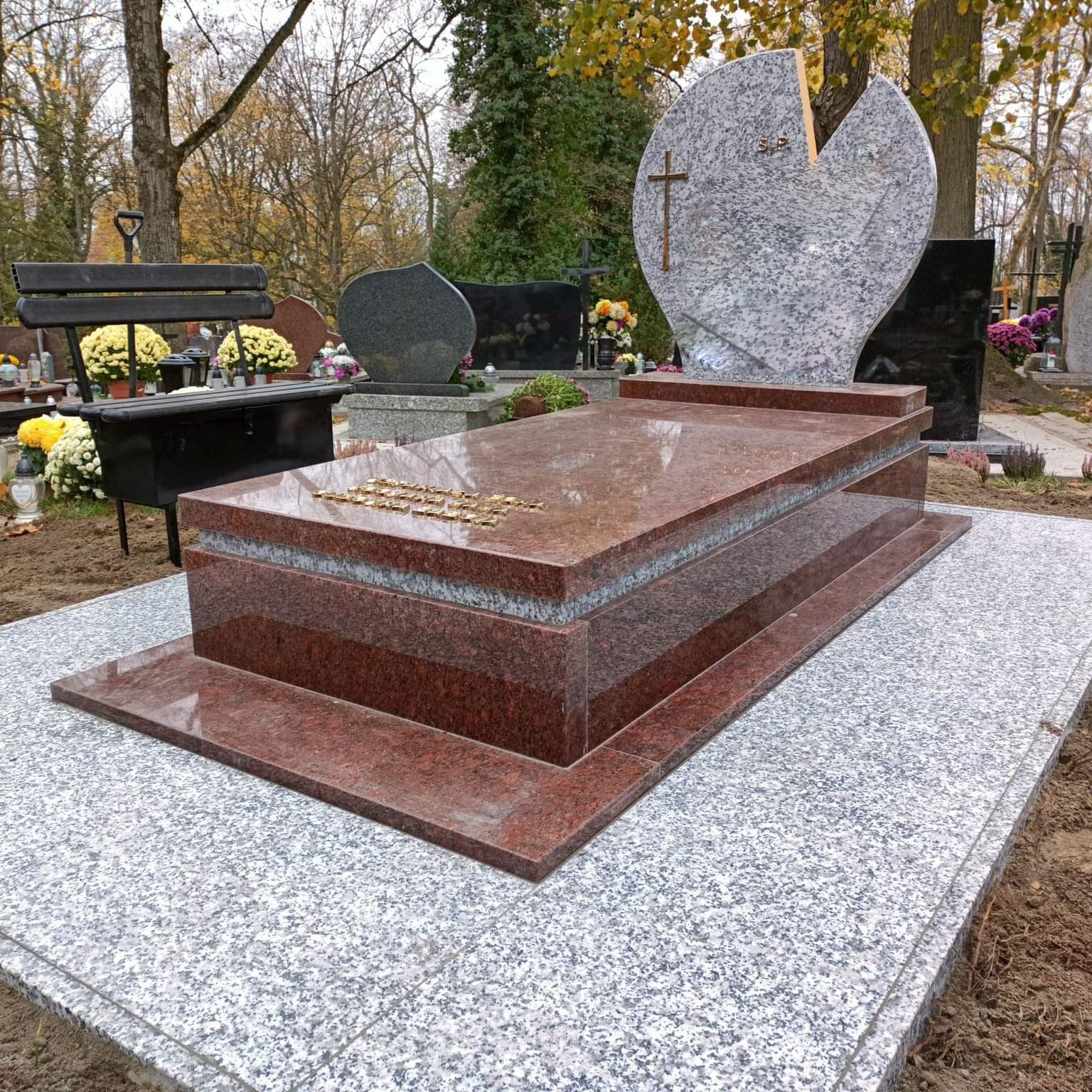 Nowoczesny, dwukolorowy pomnik z czerwonego i szarego granitu na cmentarzu, z sercowatym nagrobkiem w tle i napisem w złotych literach.