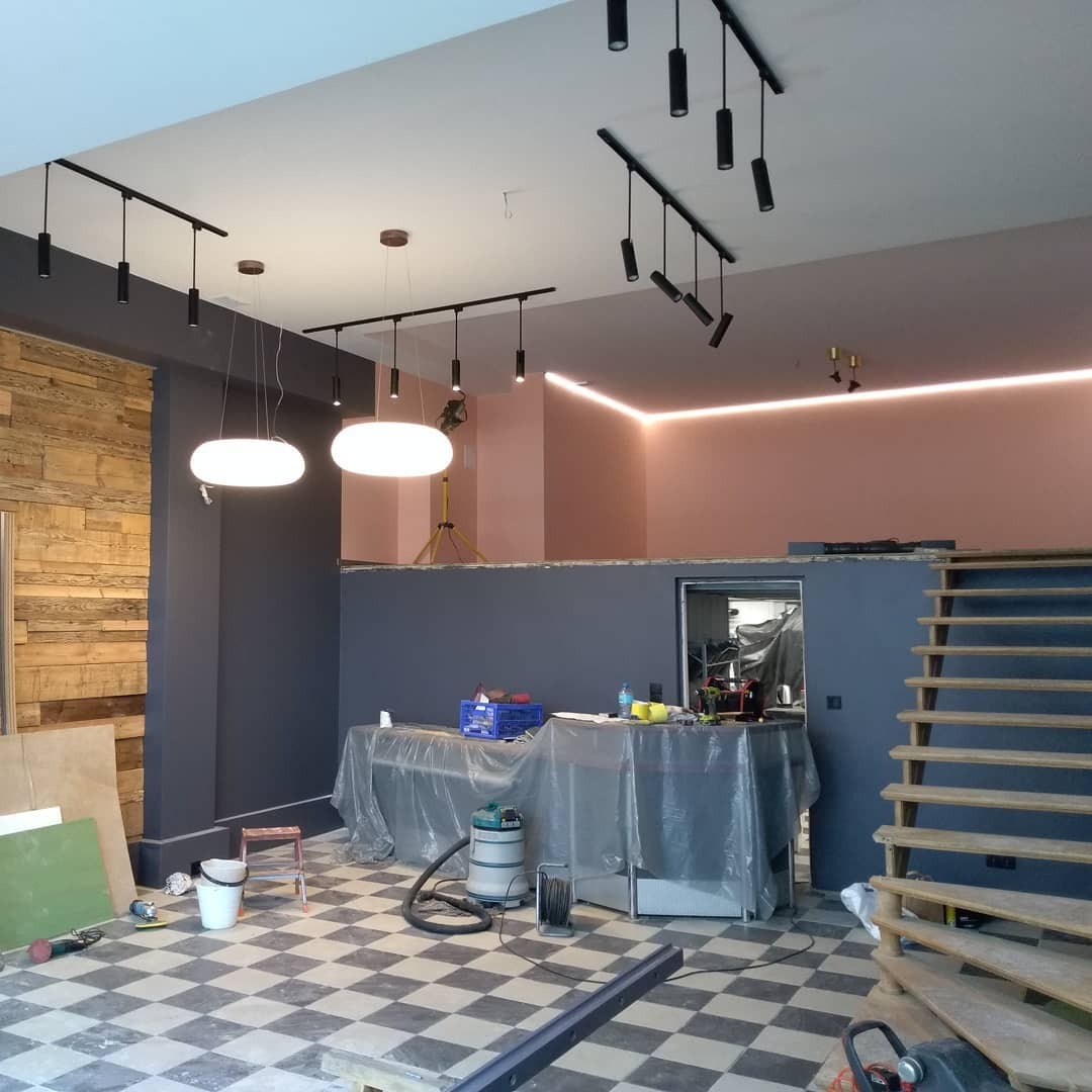 Wnętrze w trakcie remontu z zamontowanym oświetleniem szynowym z reflektorami, lampami wiszącymi i listwą LED, widoczne narzędzia i materiały budowlane na podłodze w szachownicę.