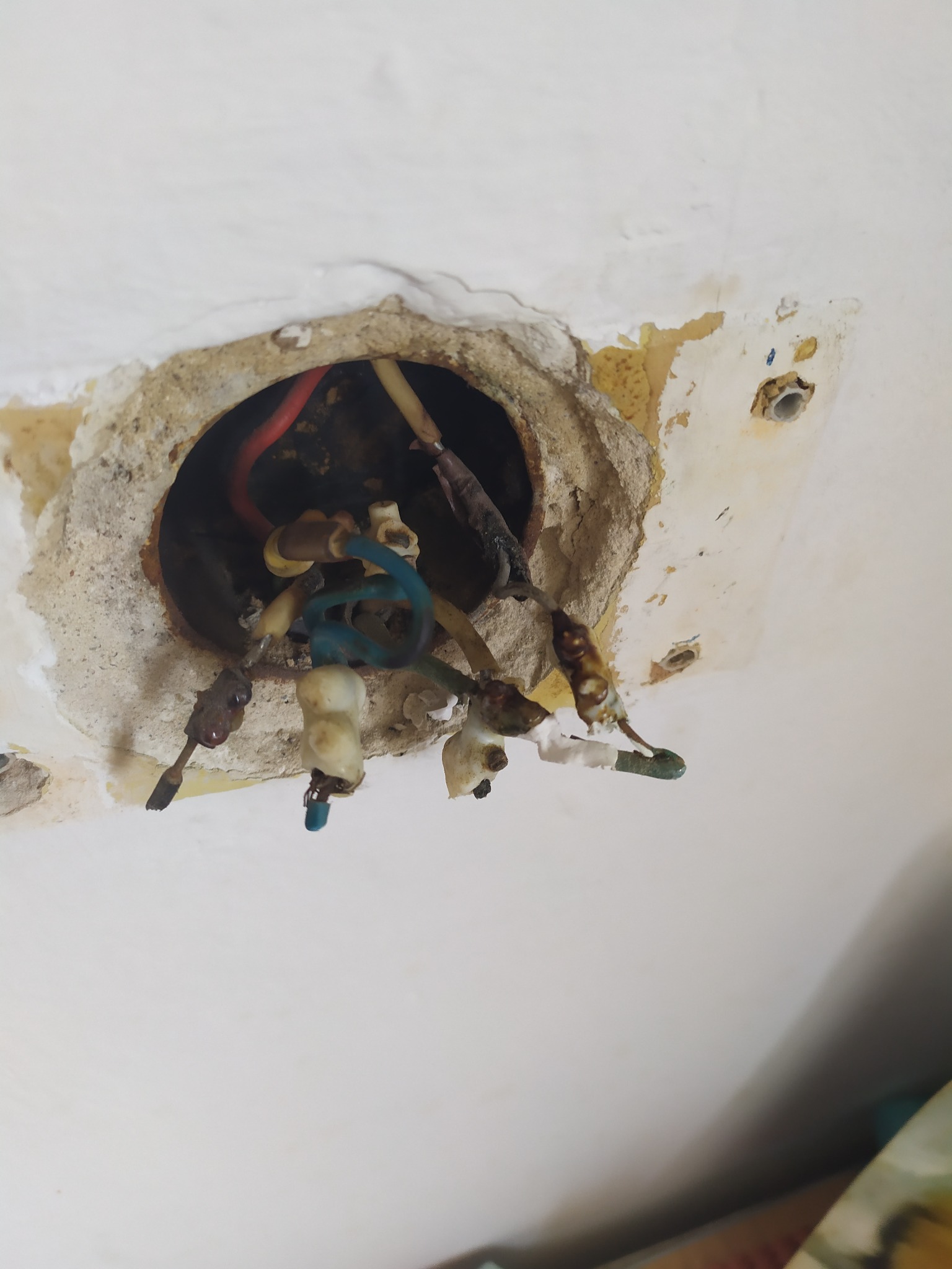 Odsłonięte, stare przewody elektryczne wystające z okrągłego otworu w suficie, z widocznymi śladami uszkodzeń i resztek farby.