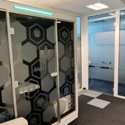 Szklane drzwi z dekoracyjnymi, matowymi wzorami w kształcie heksagonów, przedstawiającymi ikony: ciężarówka, telefon, kask, rękawice, narzędzia, budynek, uścisk dłoni, butelka, kamizelka ratunkowa,...