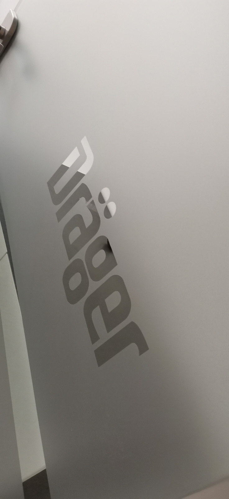 Szklana powierzchnia z naniesionym logo firmy 'Jäger' w odcieniach szarości, widoczne z boku pod kątem.