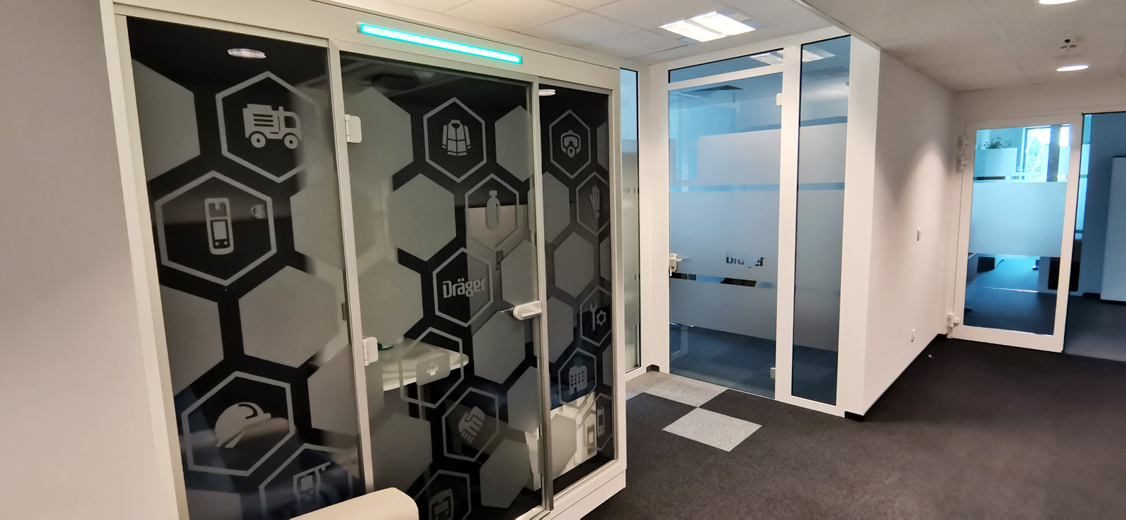 Szklane drzwi z dekoracyjnymi, matowymi wzorami w kształcie heksagonów, przedstawiającymi ikony: ciężarówka, telefon, kask, rękawice, narzędzia, budynek, uścisk dłoni, butelka, kamizelka ratunkowa,...