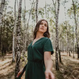 Portret kobiety w zielonej sukience, stojącej w lesie brzozowym, z delikatnym oświetleniem i naturalnym tłem.