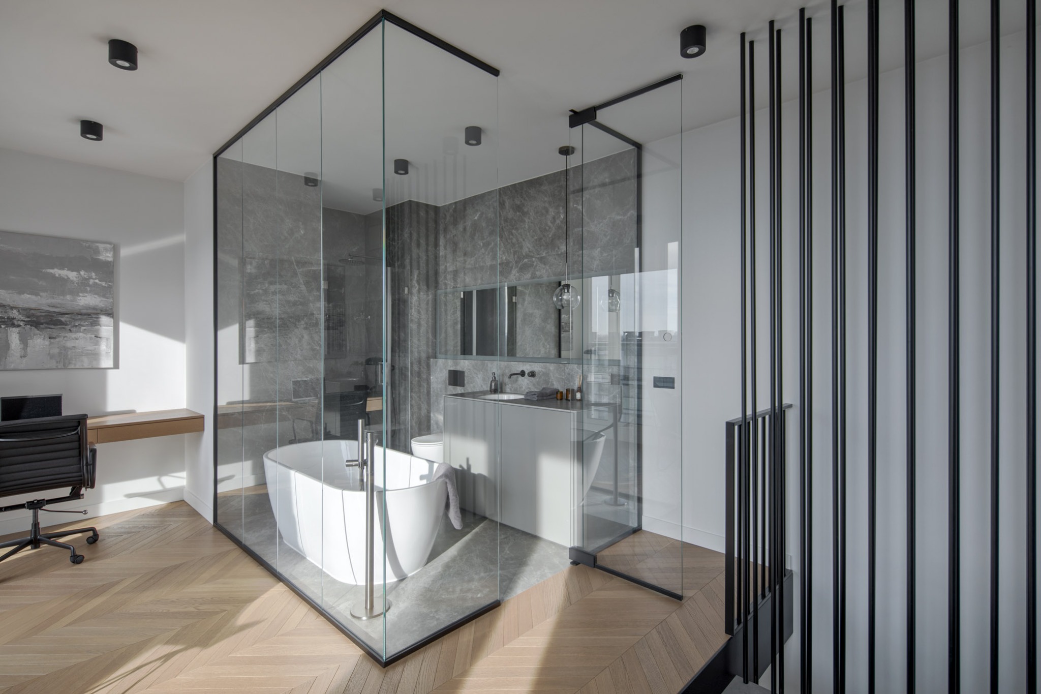 Nowoczesna łazienka z przeszkloną kabiną, wolnostojącą wanną i marmurowymi płytkami. Parkiet w jodełkę i minimalistyczne oświetlenie podkreślają elegancję.