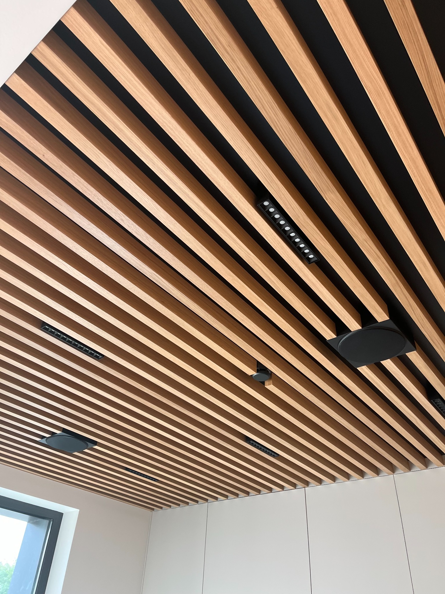 Drewniany sufit lamelowy z oświetleniem punktowym i głośnikiem, nowoczesny design wnętrza, widok z dołu, minimalistyczny styl.