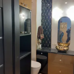 Nowoczesna łazienka z czarno-złotymi akcentami: szafka z lustrzanymi drzwiami, nablatowa umywalka w kolorze złota, czarna toaleta podwieszana i dekoracyjna ściana w romby.