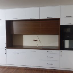 Artstyl Artur Burza - Nowoczesna zabudowa kuchenna z białymi, lakierowanymi frontami, brązowymi elementami i wbudowanym piekarnikiem oraz płytą indukcyjną, widoczne okablowanie elektryczne.