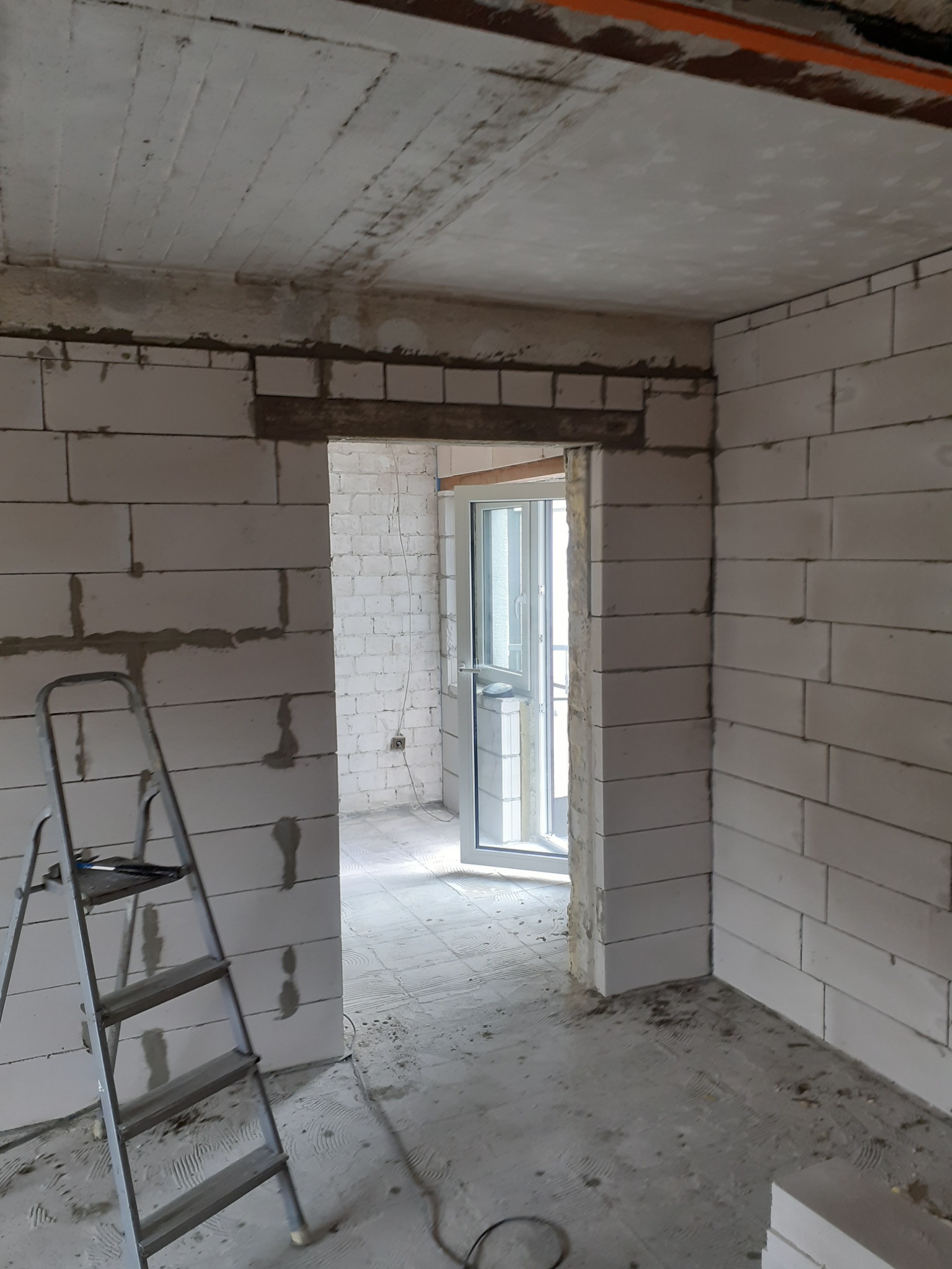 Wnętrze w trakcie budowy z widocznymi bloczkami z betonu komórkowego, surowym betonowym sufitem, aluminiową drabiną i nowymi oknami.