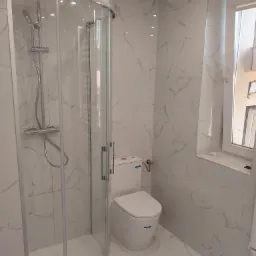 Nowoczesna łazienka z kabiną prysznicową z zaokrąglonym szkłem, toaletą kompaktową i marmurowymi płytkami na ścianach i podłodze.