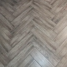 Ułożone panele podłogowe w jodełkę, imitujące drewno o jasnobrązowym odcieniu, z widoczną strukturą słoj&oacute;w.