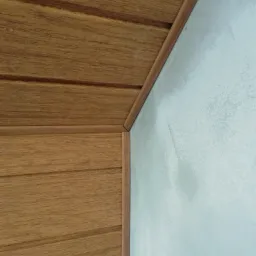 Fragment wnętrza: połączenie drewnianej boazerii na suficie i jasnej, gładkiej ściany z delikatnym efektem dekoracyjnym, wykończone drewnianą listwą narożną.