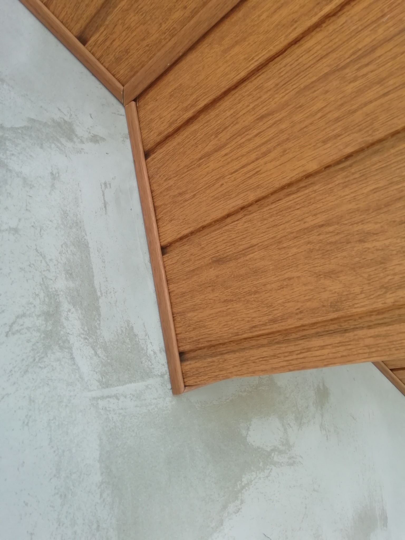 Fragment elewacji z drewnopodobnych paneli na tle surowego tynku, widoczne łączenie materiałów pod kątem.