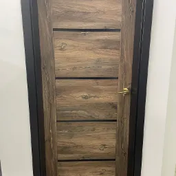 Brązowe drzwi wewnętrzne z poziomymi panelami o fakturze drewna, czarna ościeżnica, złota klamka, widoczne sęki i usłojenie.