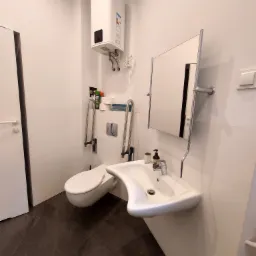 Nowoczesna łazienka z umywalką o nietypowym kształcie, wspornikami dla osób z ograniczeniami ruchowymi i podgrzewaczem wody Atlantic na ścianie.