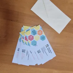 Stos wizytówek firmy Miodowa Kolonia z motywem plastra miodu i koperta na drewnianym tle.