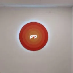 Okrągła, podświetlana tablica z logo firmy w odcieniach czerwieni, zamontowana na białej ścianie w biurze.
