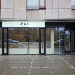 Fasada lokalu usługowego z dużymi oknami wystawowymi i szyldem 'LUKA Wilanów' nad wejściem, widok z zewnątrz na chodnik i ulicę.