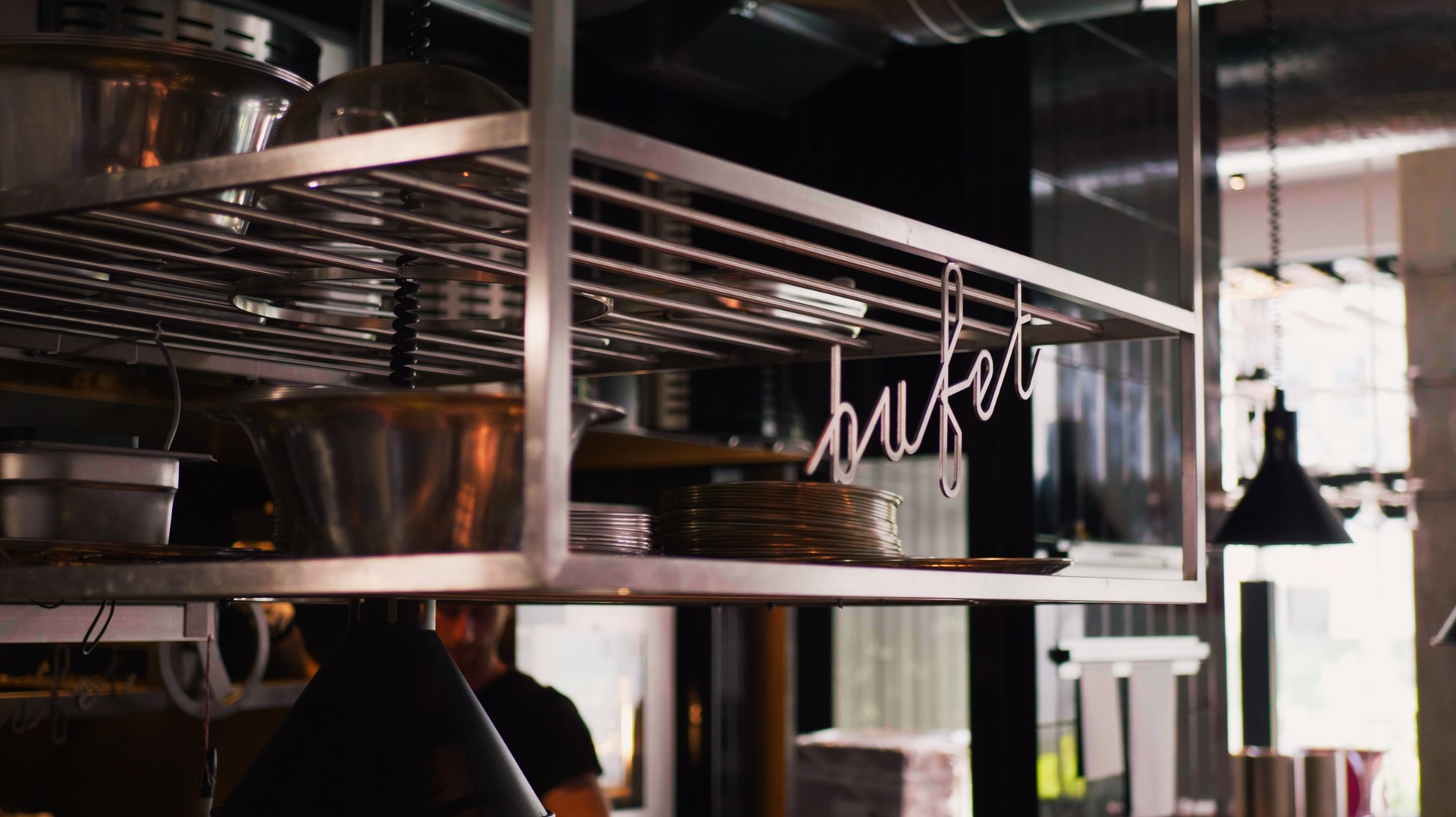 Metalowa półka w restauracji z naczyniami i dekoracyjnym napisem 'bufet'.