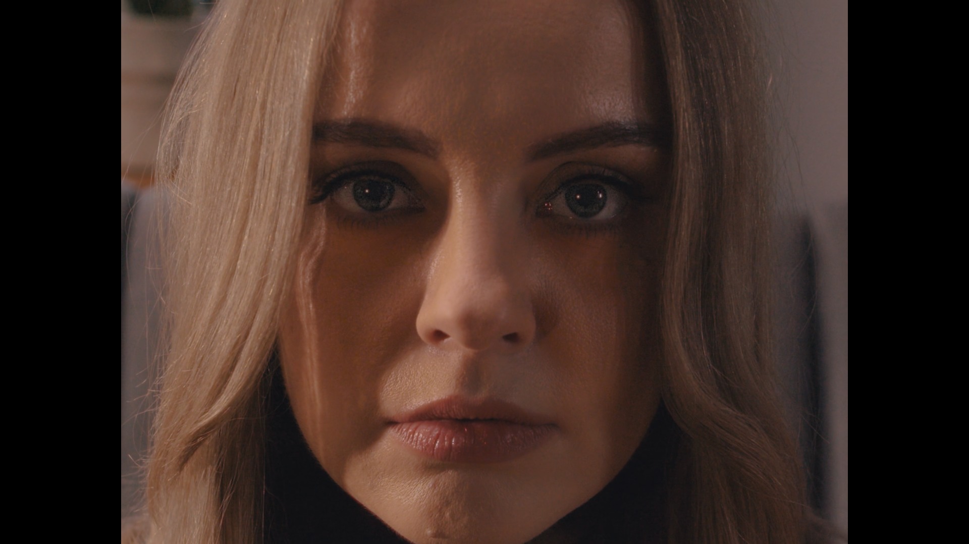 Portret kobiety z bliska, z naciskiem na wyraziste spojrzenie i delikatne oświetlenie, sugerujące kadr z filmu lub sesji zdjęciowej.