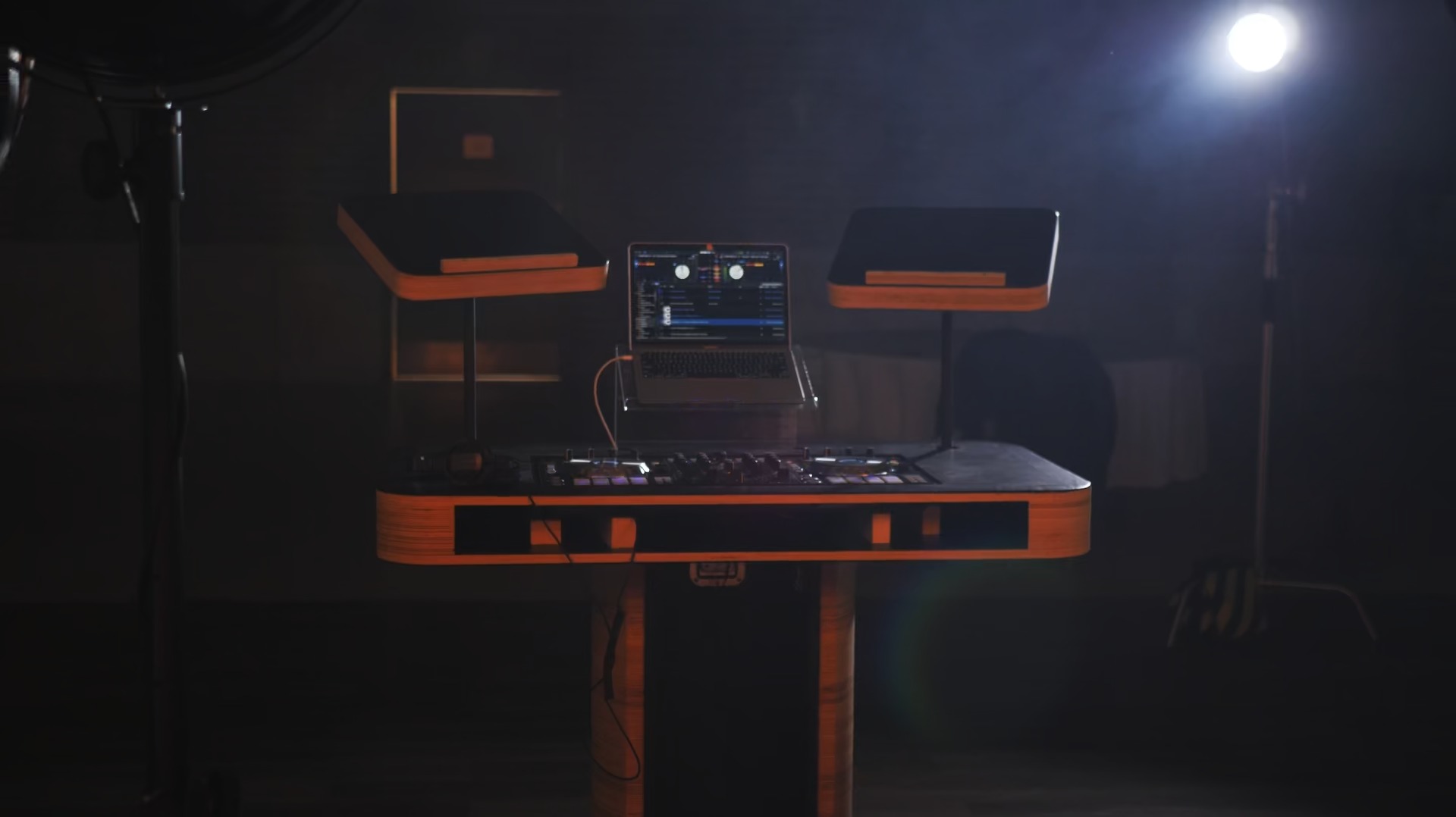 Stanowisko DJ-a z laptopem i kontrolerem, oświetlone studyjnymi lampami w ciemnym pomieszczeniu.